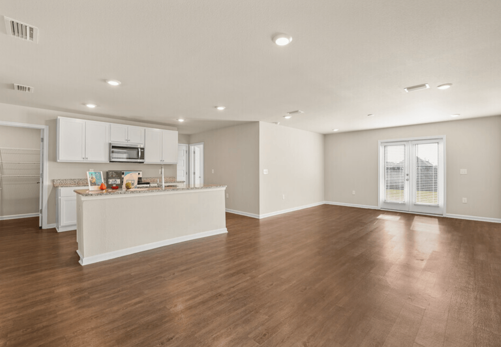 the living room and kitchen of a new home with wood flooring and white cabinets