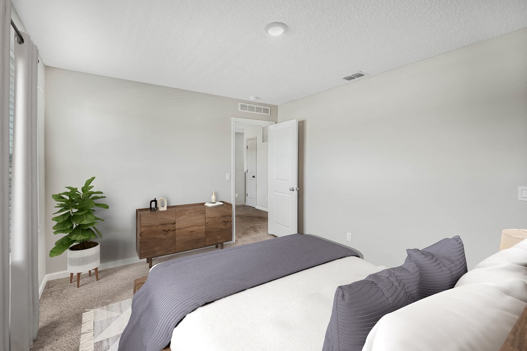 A bedroom with a bed, nightstand, and a plant.