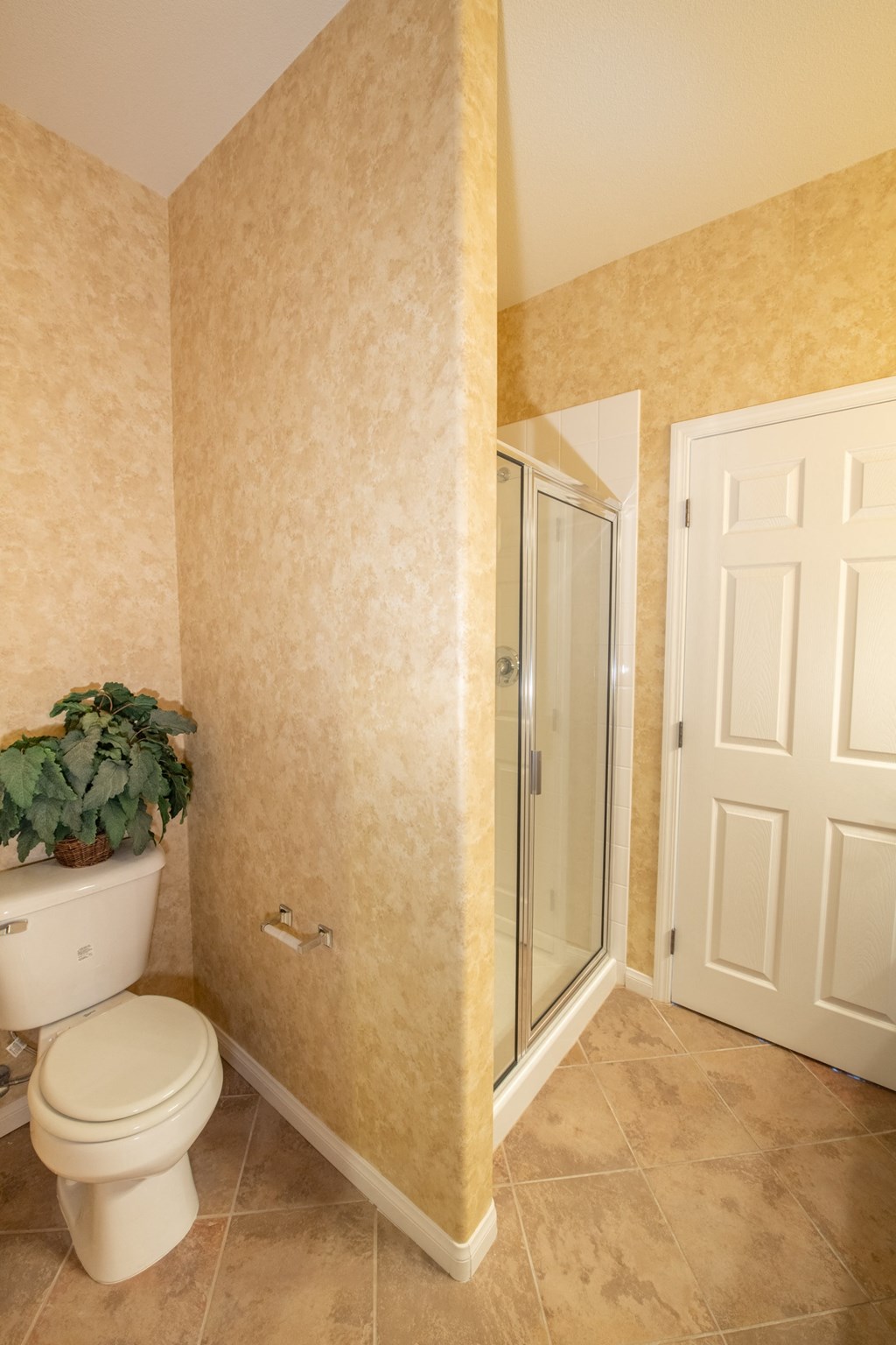 a bathroom with a toilet and a shower and a potted plant