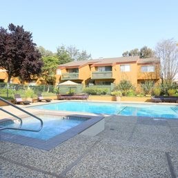 A swimming pool in front of a building with a green lawn and trees.