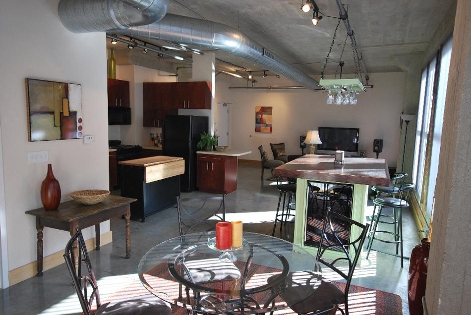 a room with a table and chairs and a kitchen in the background