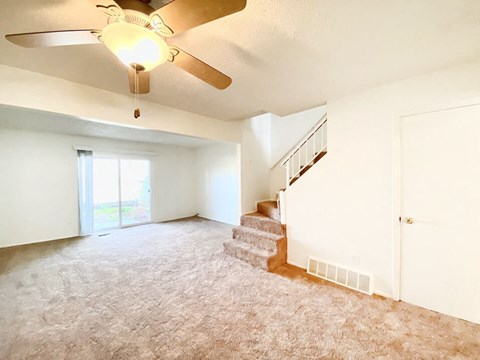 an empty living room with a ceiling fan and stairs