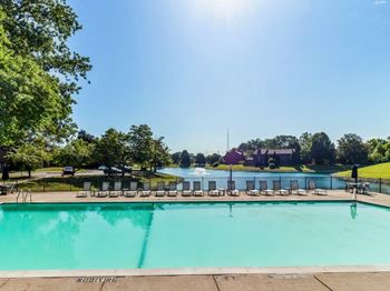 a swimming pool with chaise lounge chairs and a body of water in the background