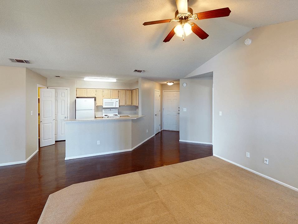 a living room with a ceiling fan and a kitchen in the background