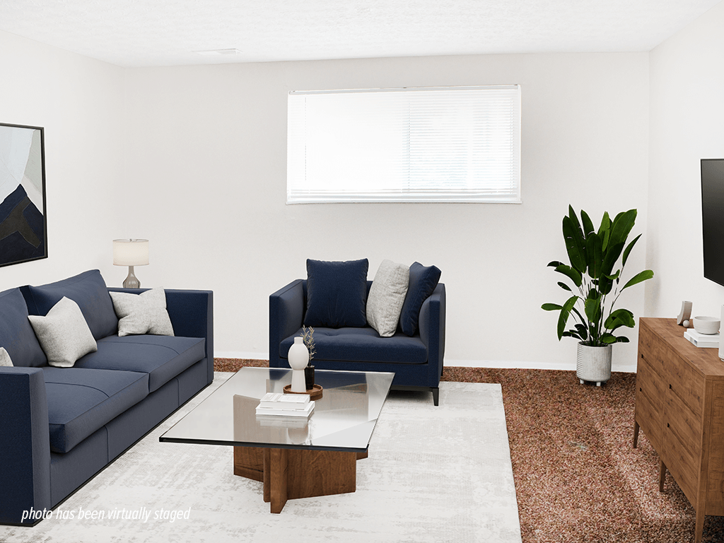 A living room with a blue couch, a blue chair, a glass coffee table, a rug, a plant, and a TV.