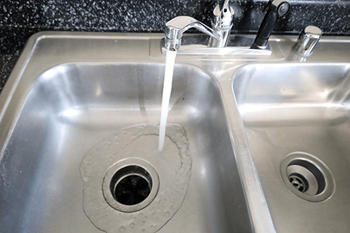 A silver sink with a drain plug and running water.