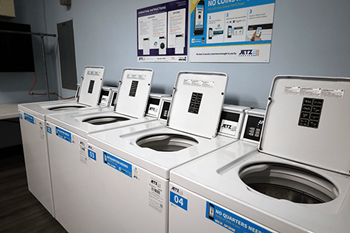 A row of washing machines with the sign "No Quarters Needed" on the wall.