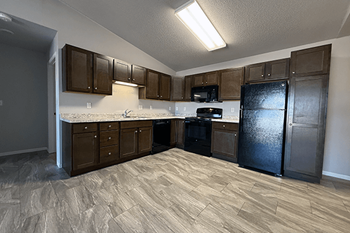 A kitchen with a black refrigerator, brown cabinets, and a white countertop.