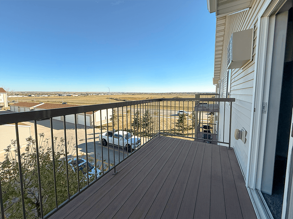 A balcony with a wooden floor and a metal railing overlooking a parking lot.