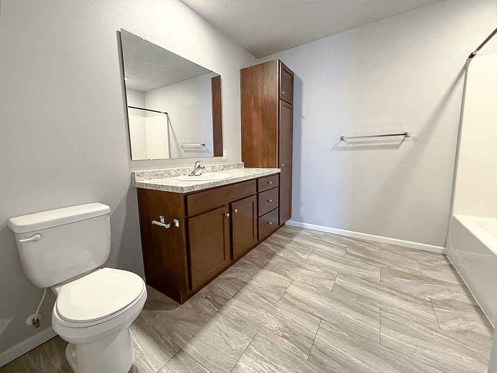 A bathroom with a toilet, sink, and wooden cabinets.