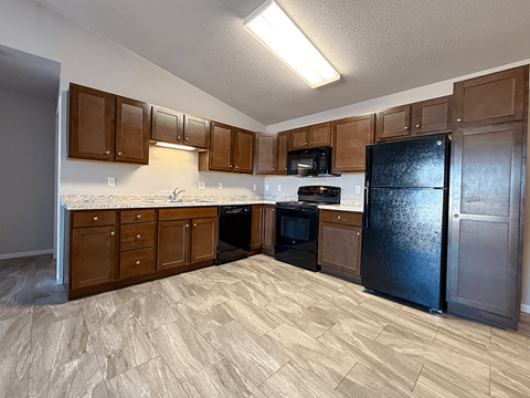 A kitchen with wooden cabinets and a black refrigerator.