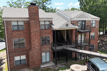 A red brick apartment building with a balcony and a car parked in front.