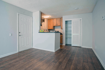 an empty living room with a kitchen in the background