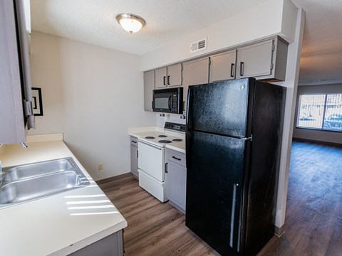A black refrigerator stands in a kitchen with a stainless steel sink.