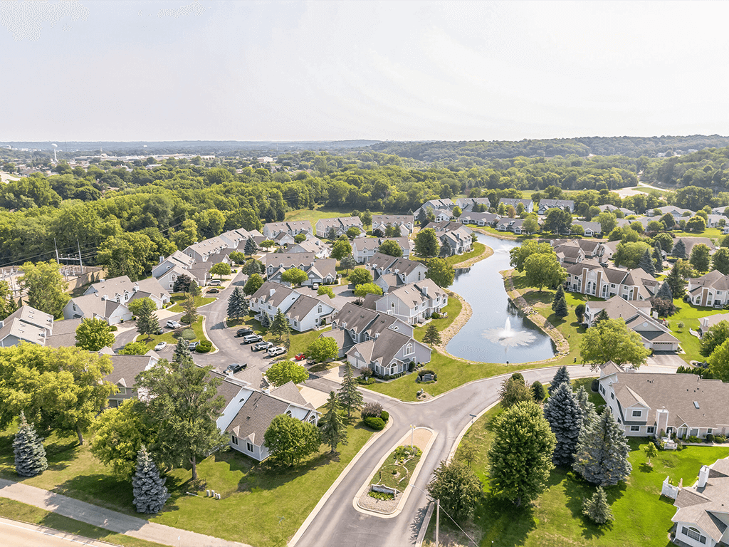 A bird's eye view of a residential neighborhood with houses, a pond, and a winding road.