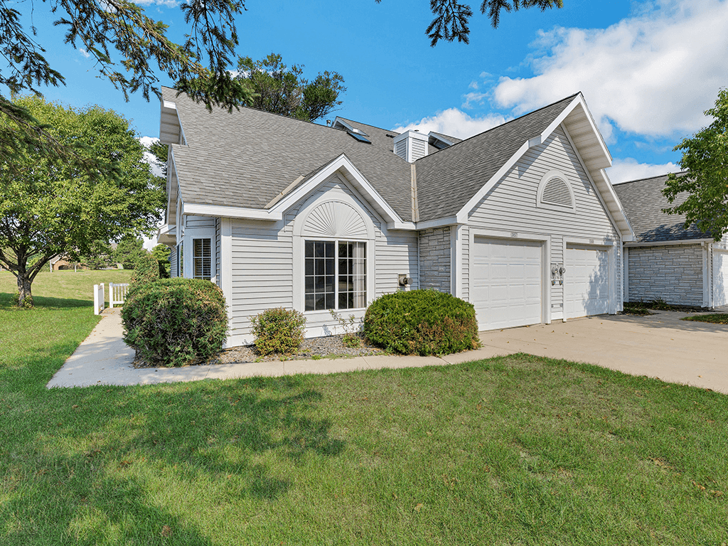 A house with a grey roof and white walls is surrounded by a well-kept lawn.