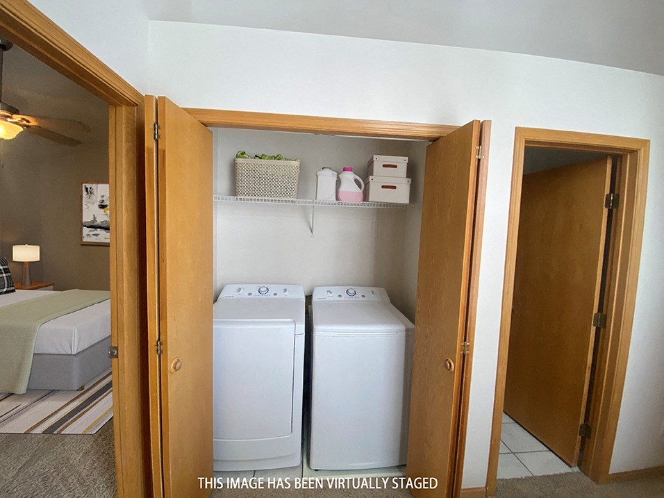 a closet with two washer and dryers and a bed in the background