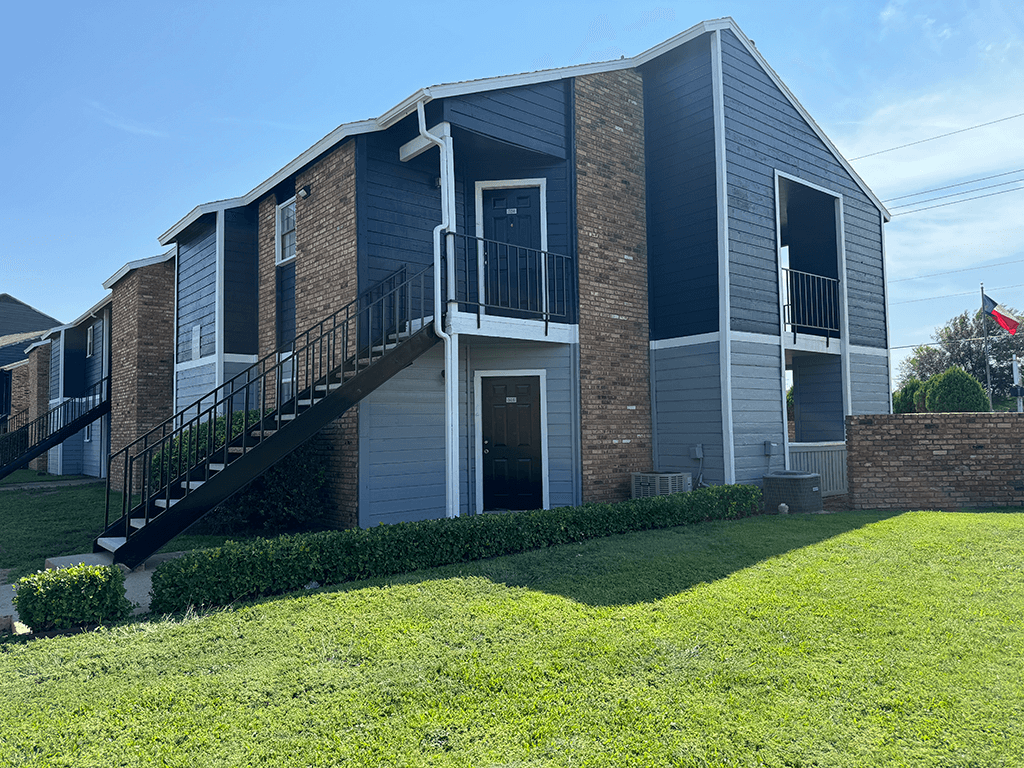 an apartment building with a green lawn and a staircase