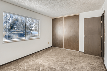 A room with a carpeted floor, a window with blinds, and a door.