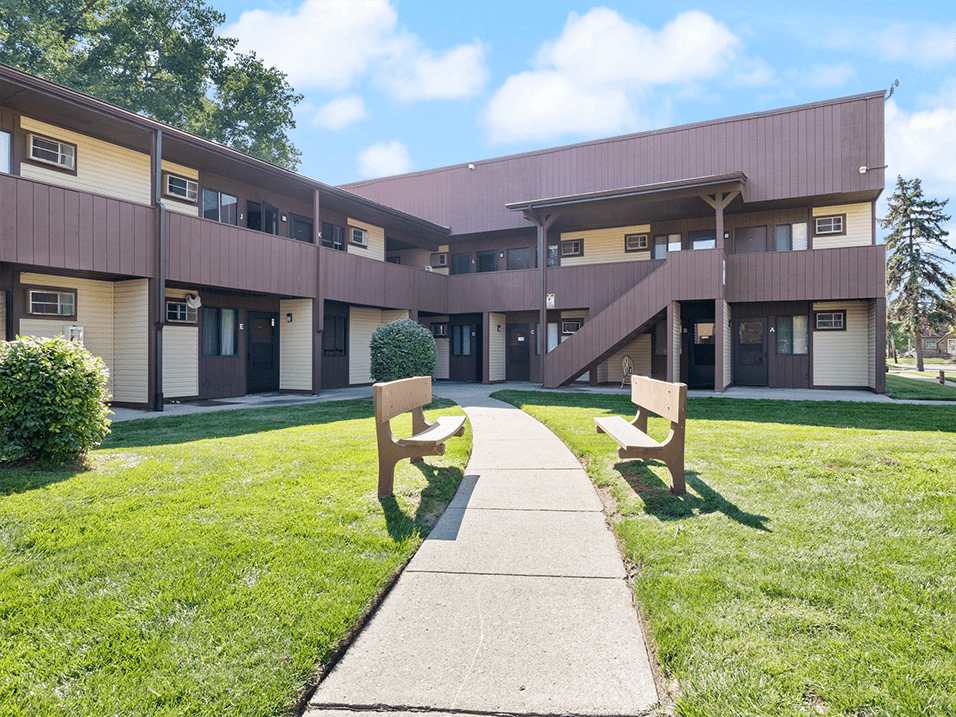a sidewalk in front of a apartment building with benches