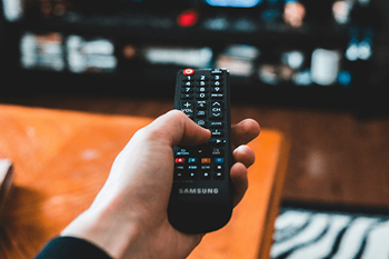 A person is holding a Samsung remote control in front of a television.