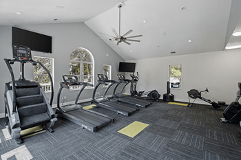 A spacious gym with treadmills, elliptical machines, and a ceiling fan.