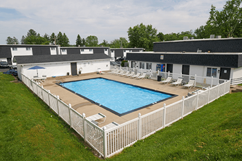 an aerial view of a resort style pool in front of a white fence