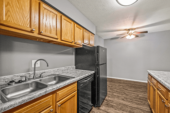 A kitchen with a black refrigerator, wooden cabinets, and a marble countertop.