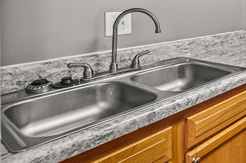A kitchen sink with a marble countertop and wooden cabinets.