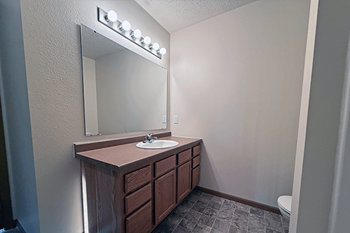 A bathroom with a vanity and a mirror with lights above it.