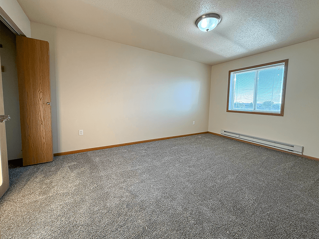 A room with a carpeted floor, a window with blinds, and a door.