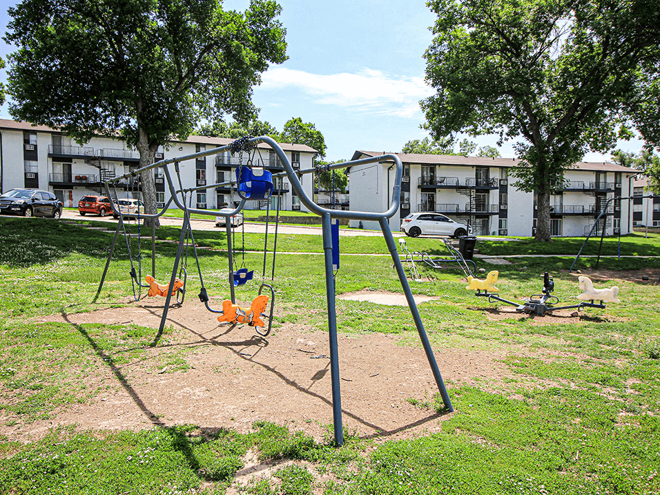 a swing set in a park with apartment buildings in the background