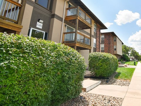 an apartment building with a sidewalk and hedges in front of it
