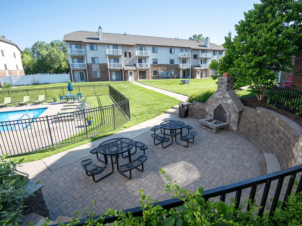 an outdoor patio with picnic tables and a pool in front of an apartment building