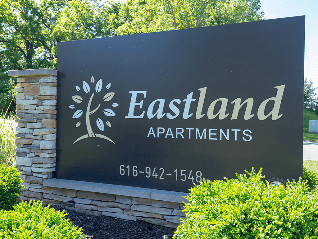 a stone monument sign for eastland apartments with trees in the background