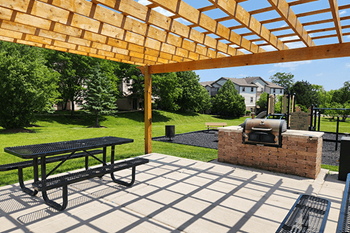 A picnic table is under a wooden pergola with a grill.