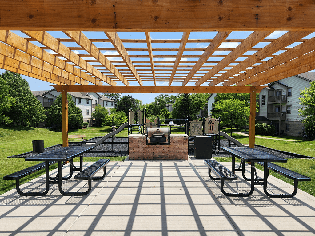 A wooden pergola over a picnic table in a park.