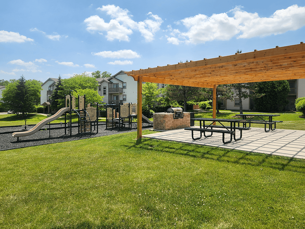 A playground with a slide, swings, and picnic tables under a wooden canopy.