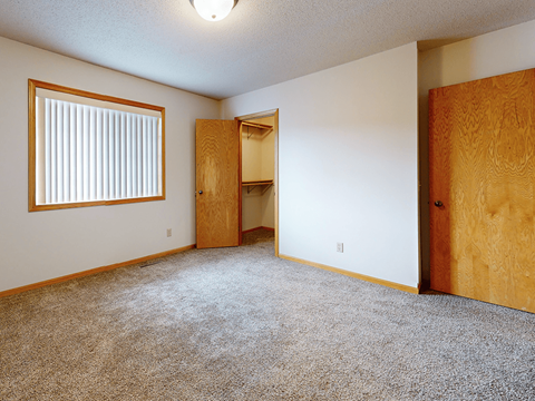 A room with a carpeted floor, a window with blinds, and a wooden door.