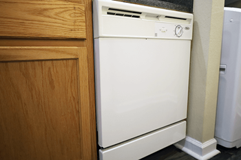 A white dishwasher is placed next to a wooden cabinet.