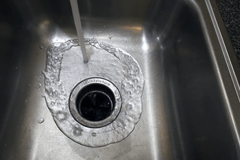 A silver sink with a drain and water running out of it.