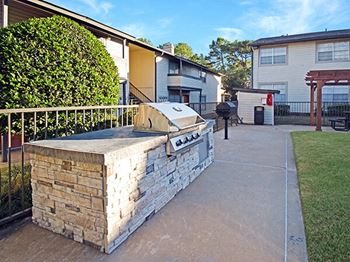 A stone wall with a grill on top is in the foreground of a residential area.