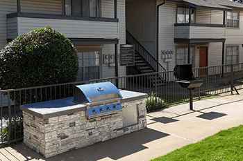 A stone BBQ grill is in front of a building.