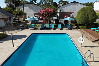 A blue swimming pool in a backyard with a deck and chairs.