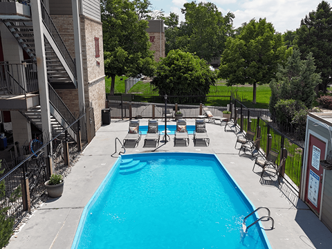 A pool surrounded by chairs and trees.