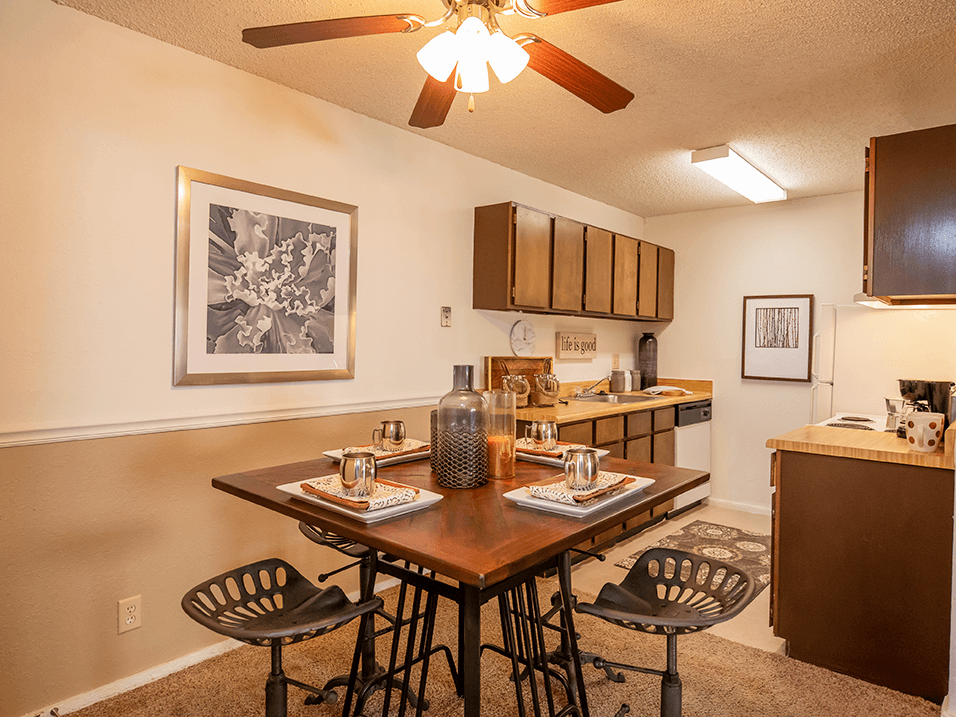 a dining area with a table and chairs and a kitchen in the background