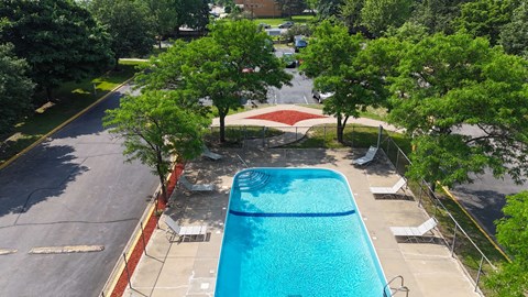 A swimming pool surrounded by trees and a parking lot.