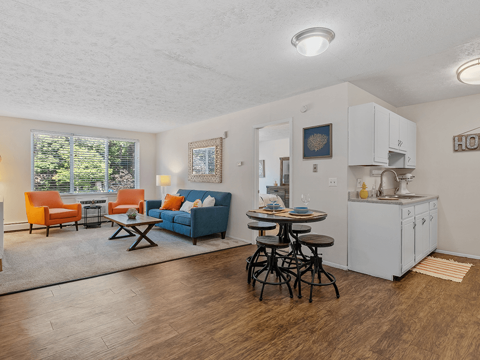 a living room with a couch a table and a chair and a kitchen with a sink and