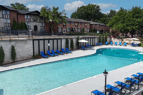 A swimming pool surrounded by blue lounge chairs and a brick building.