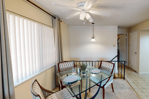 A glass dining table with four chairs and a ceiling fan.